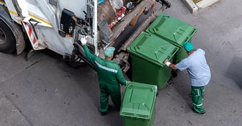 Two men loading garbage into a garbage truck.