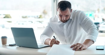 A car salesman in his office at a car dealership reviewing printed reports.