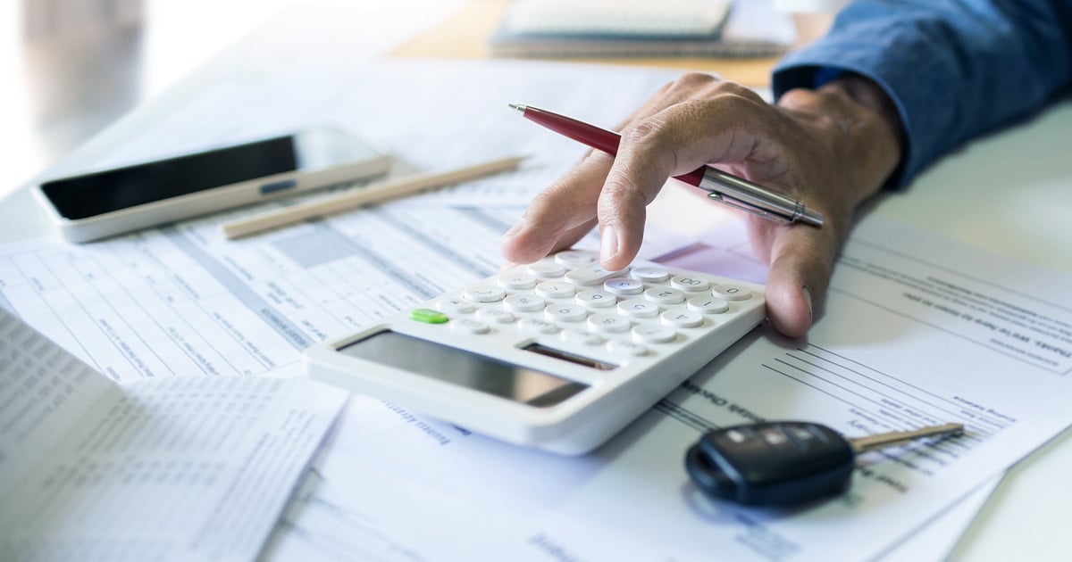 Close up of a person using a calculator to work on dealership finances.