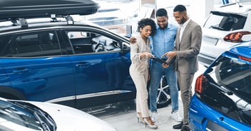 Couple Visiting Car Dealership Talking With Salesman In Auto Showroom