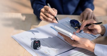 Close up of a a car dealer looking at paperwork with a client.