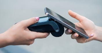 Person using contactless payment by holding smartphone near a card reader terminal with both hands visible