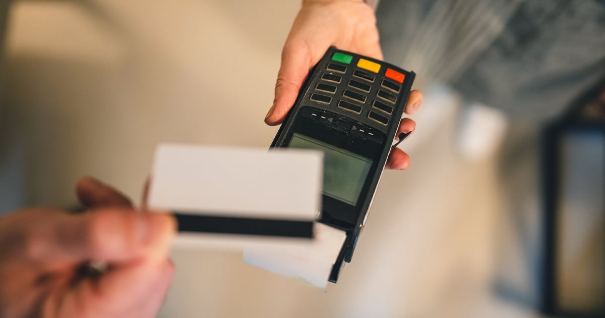 Close up of a person holding a handheld payment terminal with another person reaching out to tap their card.