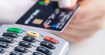 Close-up of POS system keypad with colorful function buttons and black credit card held by hand in background.