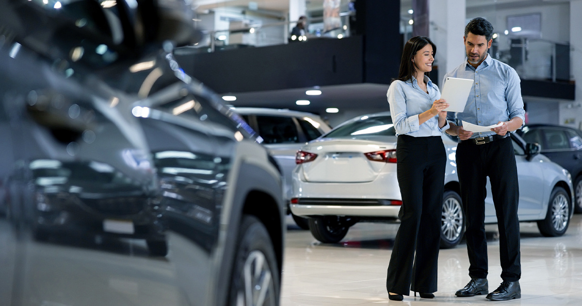 Two salespeople working together at a car showroom and reading on a tablet